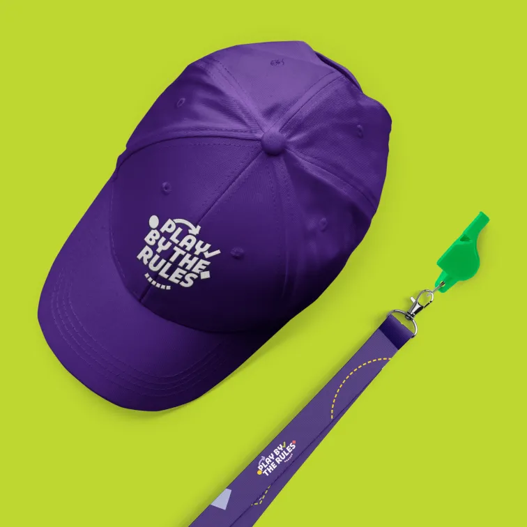A Play by the Rules branded cap and lanyard on a lime coloured background. The lanyard has a green whistle